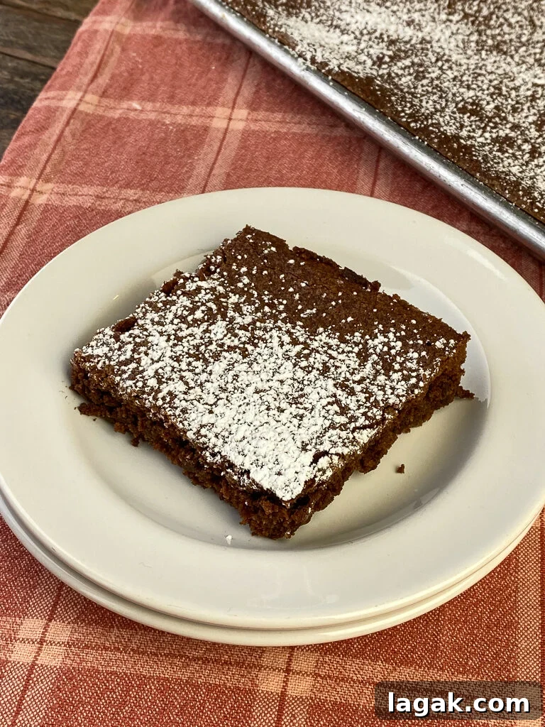 Overhead view of a large brownie next to a big baking sheet full of brownies with confectioners sugar