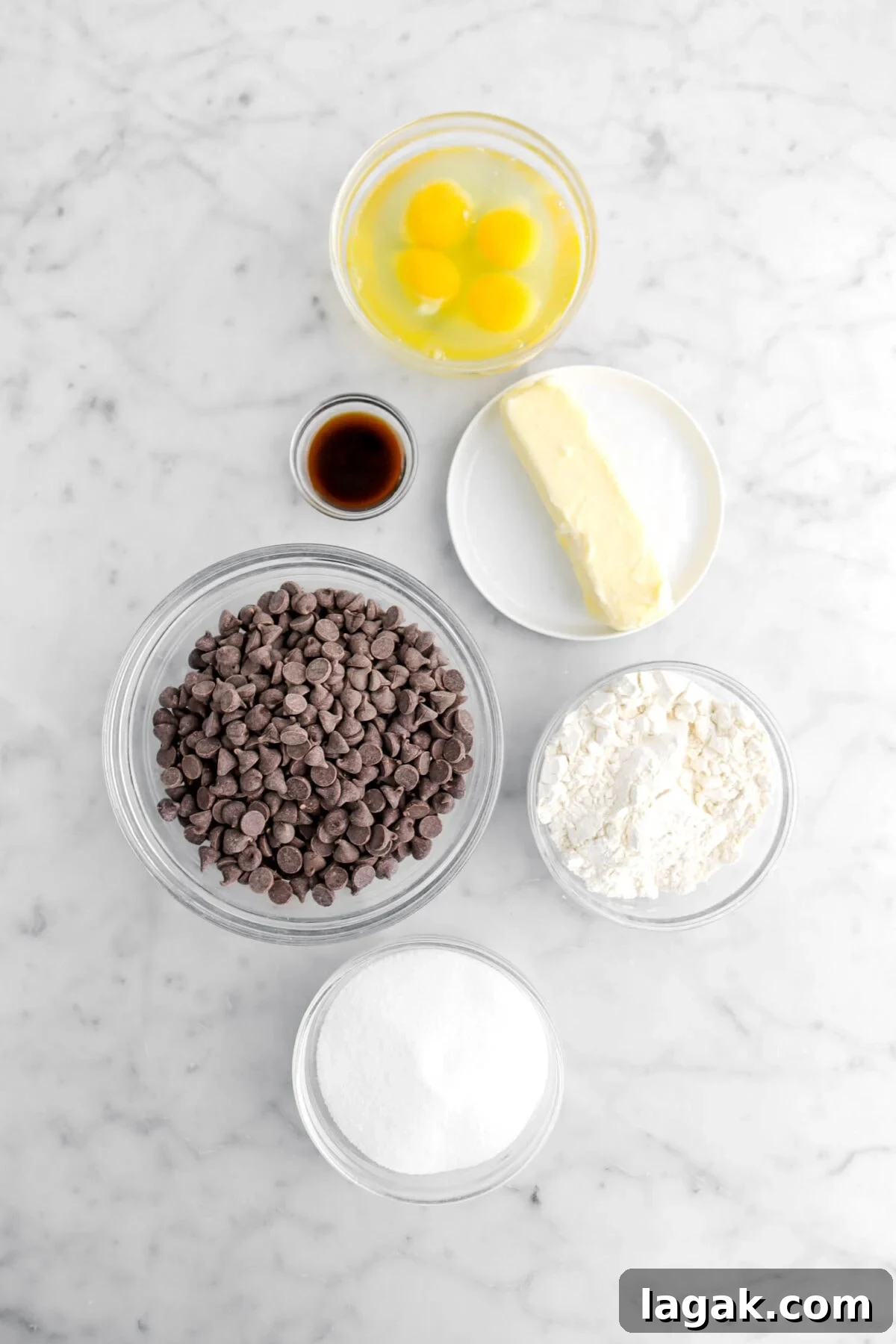 eggs, vanilla, butter, chocolate chips, flour, and sugar on marble surface.