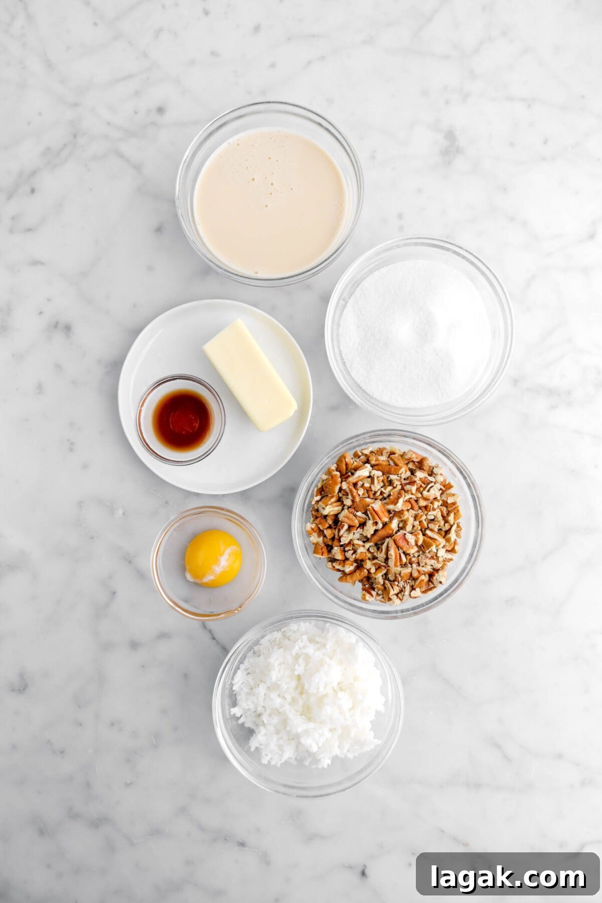 Evaporated milk, sugar, butter, vanilla, chopped pecans, egg yolk, and shredded coconut on marble surface.