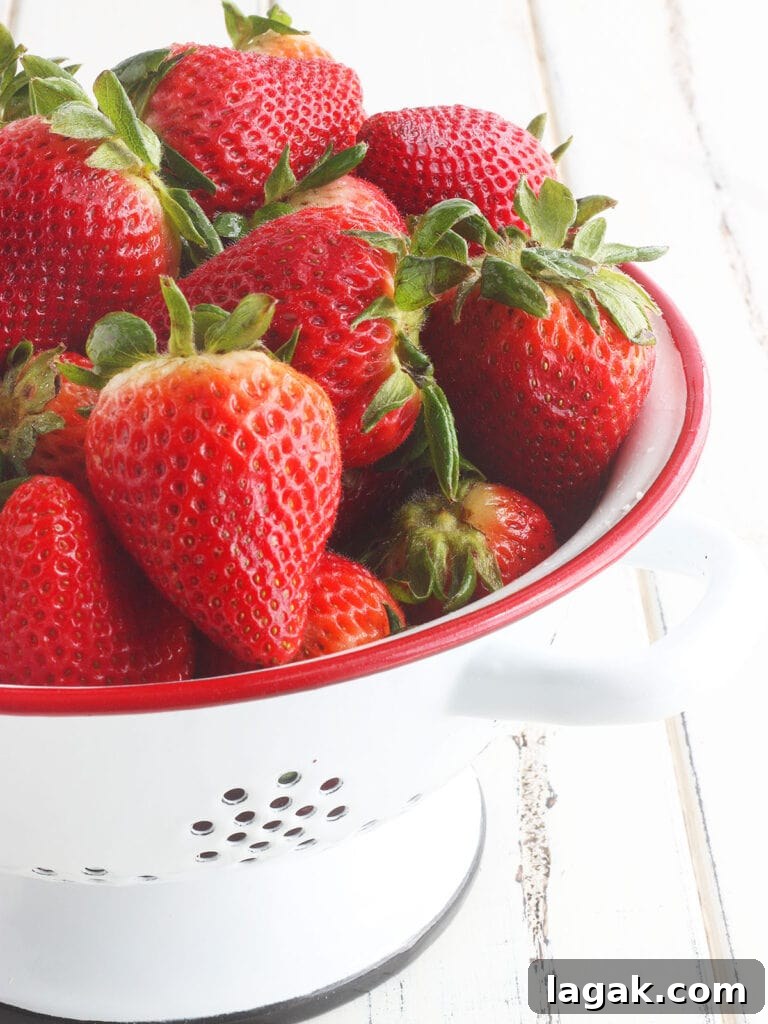 Strawberry Jam Recipe with Pectin: Smooth, Spreadable Preserves 4 Whole fresh strawberries in a red and white colander.