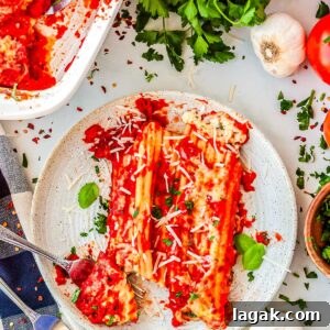 Creamy Three-Cheese Manicotti with Homemade Tomato Sauce 12 A plated serving of two manicotti rolls covered in red sauce and cheese, cut open with a fork to show the white ricotta filling inside.
