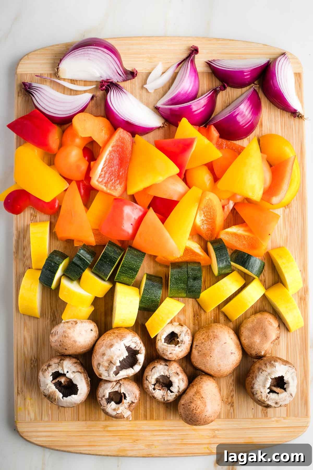 Cutting board with big chunks of red onion, bell peppers, zucchini, yellow squash and baby bella mushrooms.