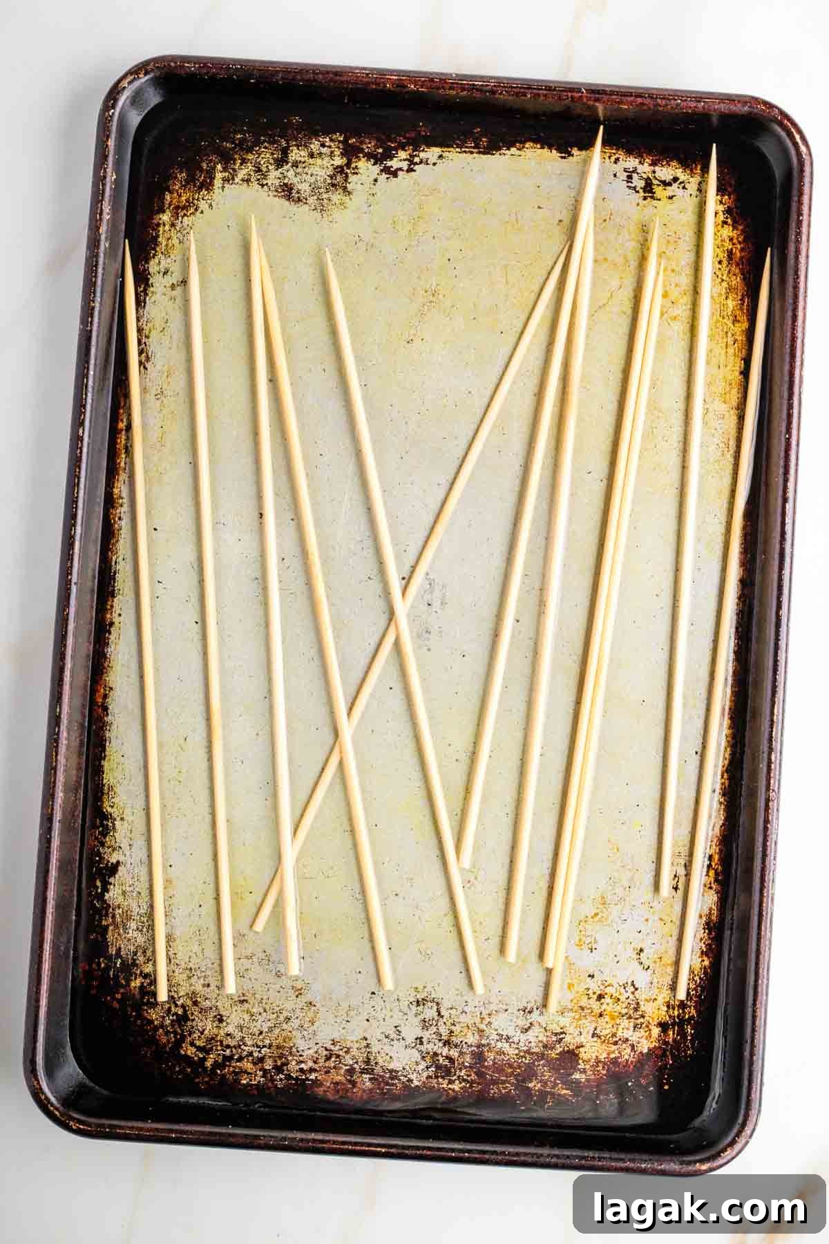 Bamboo skewers soaking in water on a rimmed baking sheet.