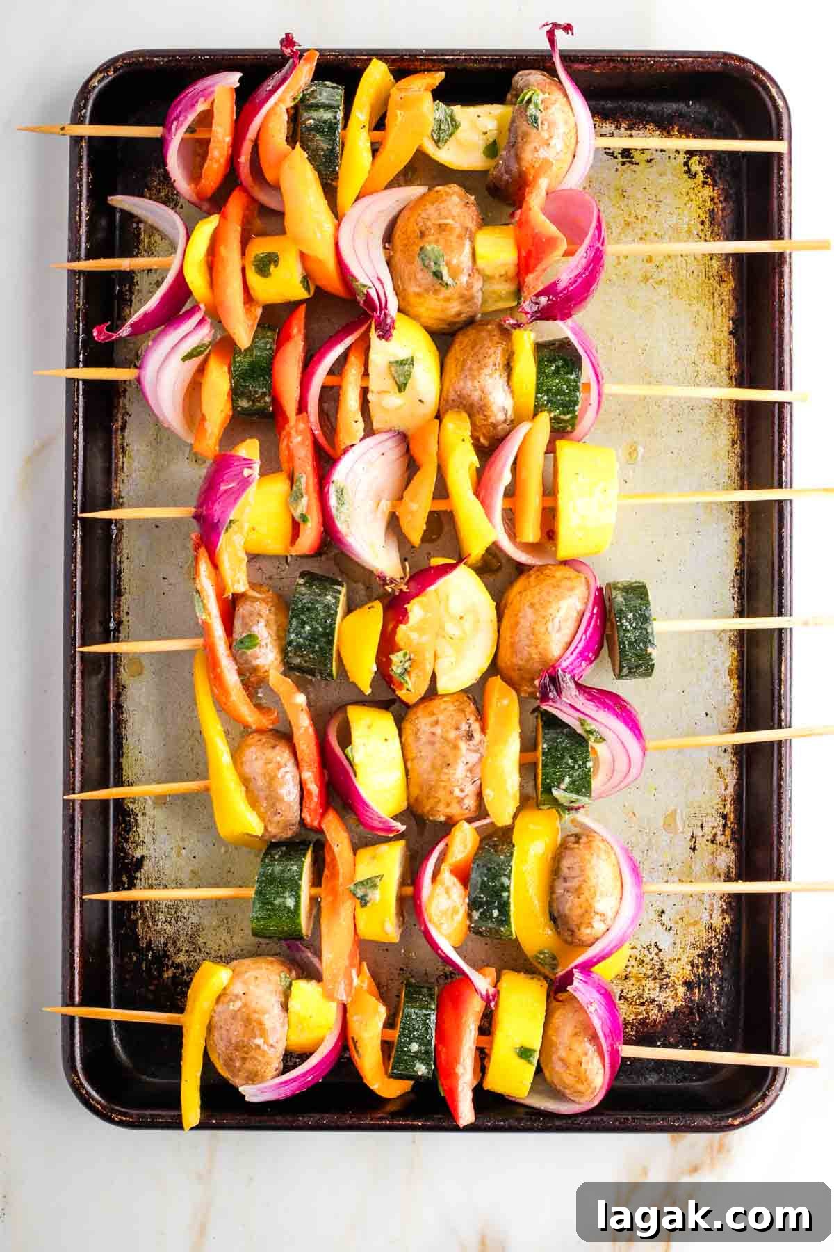 Colorful vegetable chunks on bamboo skewers stilling on a rimmed baking sheet.