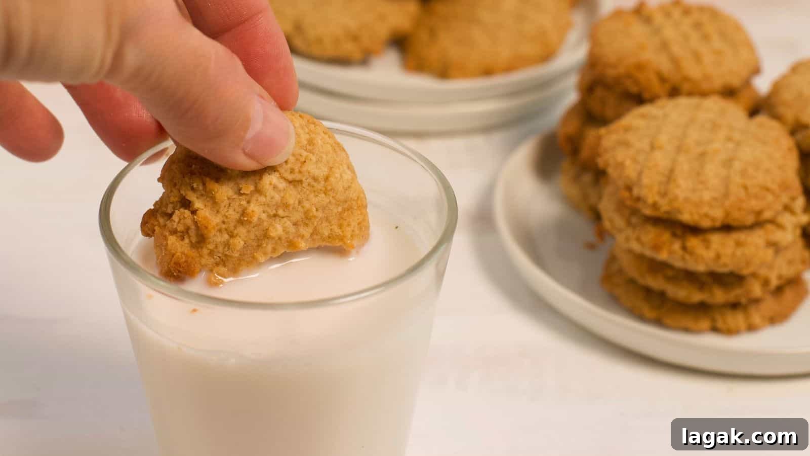 29 Party-Worthy Treats That Won’t Leave Leftovers 17 A person dipping a peanut butter cookie into a glass of milk, with more stacked cookies on a plate in the background.