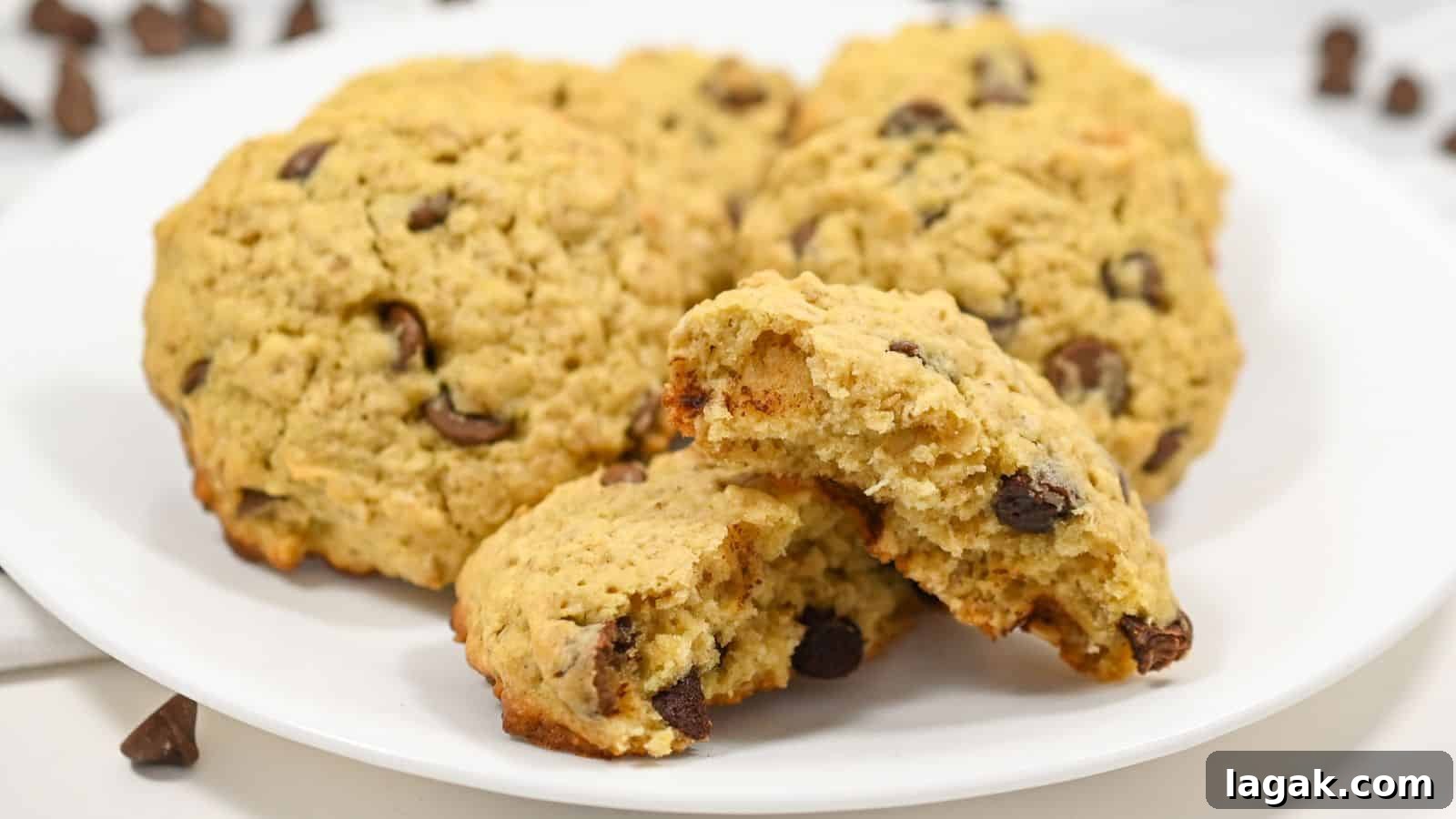 29 Party-Worthy Treats That Won’t Leave Leftovers 21 Chocolate oatmeal cookies on a white plate, one broken in half, showing a soft interior, with loose chocolate chips scattered around on a white surface.