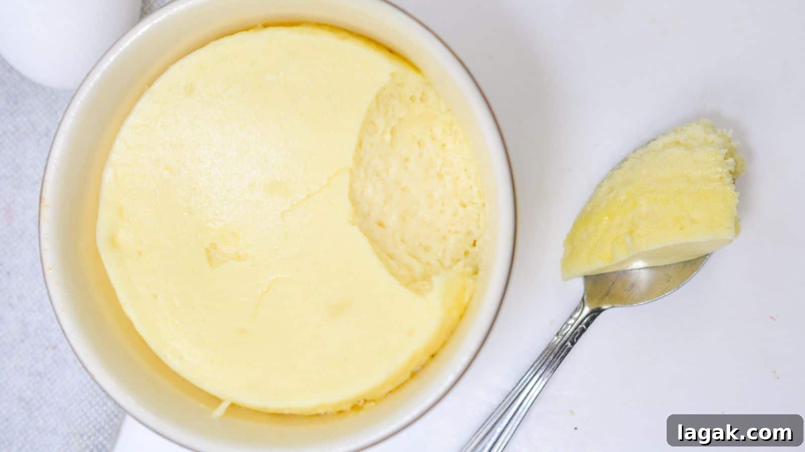 29 Party-Worthy Treats That Won’t Leave Leftovers 26 A ramekin of creamy, smooth cheesecake with a spoon resting beside it, taking out a scoop on a white background.