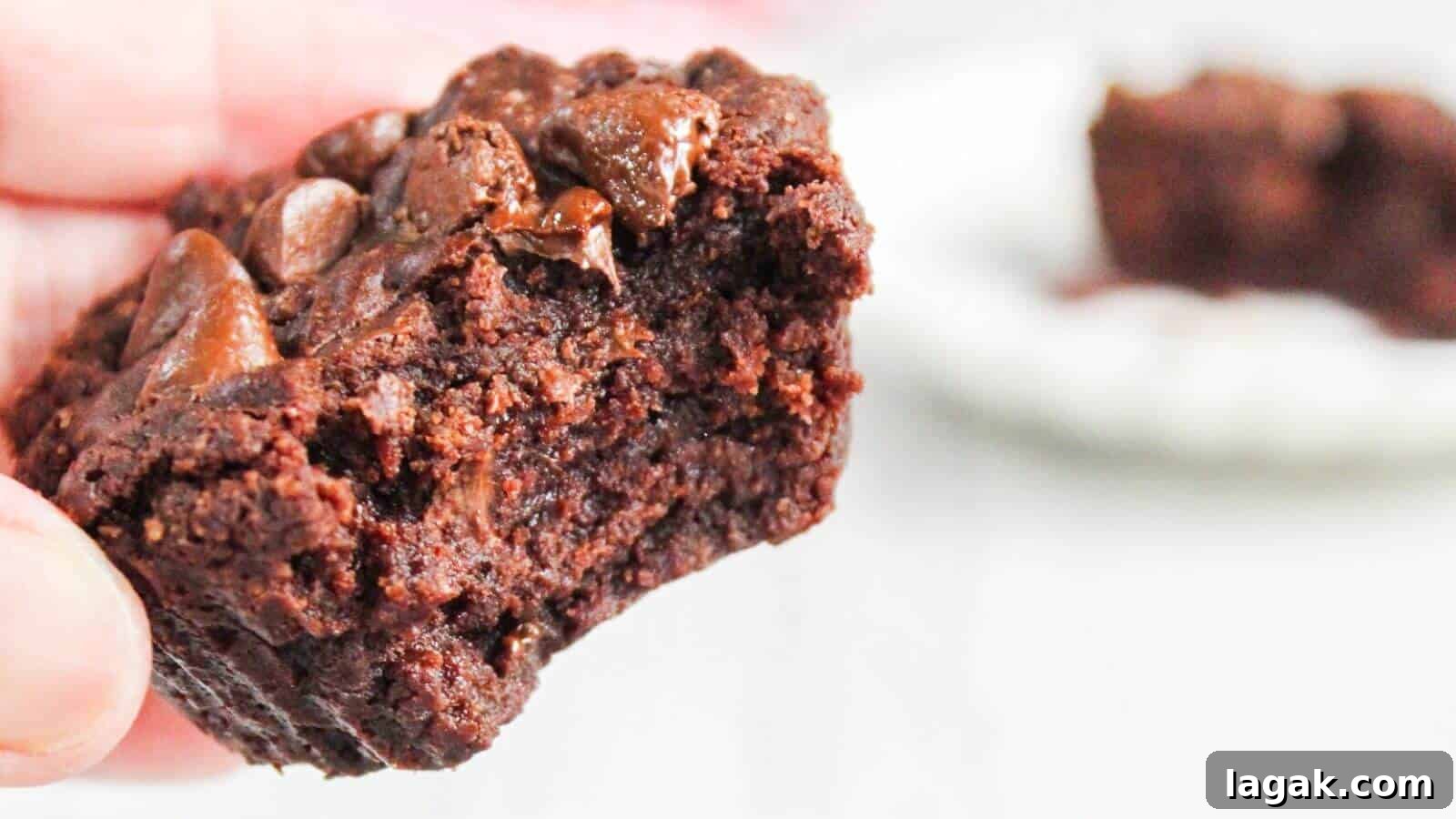 29 Party-Worthy Treats That Won’t Leave Leftovers 28 Close-up of a hand holding a half-eaten chocolate brownie with gooey chocolate chunks, with another partial brownie blurred in the background.