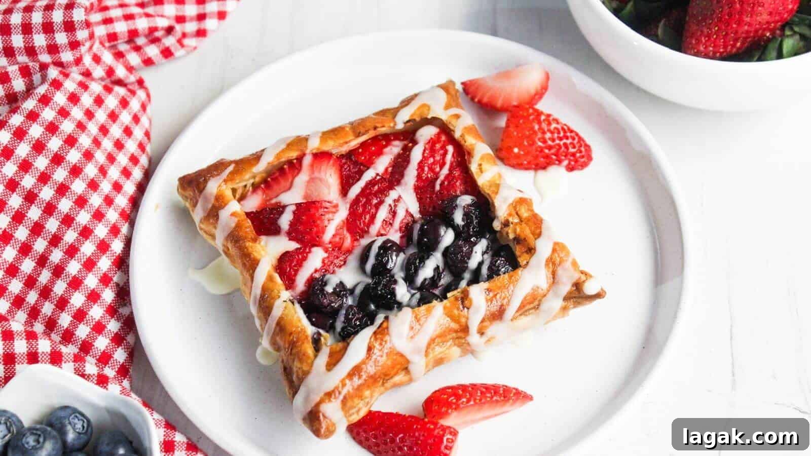 29 Party-Worthy Treats That Won’t Leave Leftovers 8 A pastry with berry filling and white drizzle on a white plate is accompanied by strawberry slices. A red and white checkered cloth, blueberries, and a bowl of strawberries are nearby.