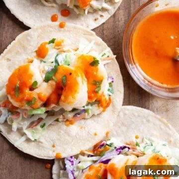a close up view of bang bang shrimp tacos on a wooden board next to a bowl of bang bang sauce.