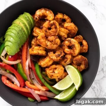 a top down view of a serving bowl with shrimp, sautéed veggies, sliced avocado and limes.