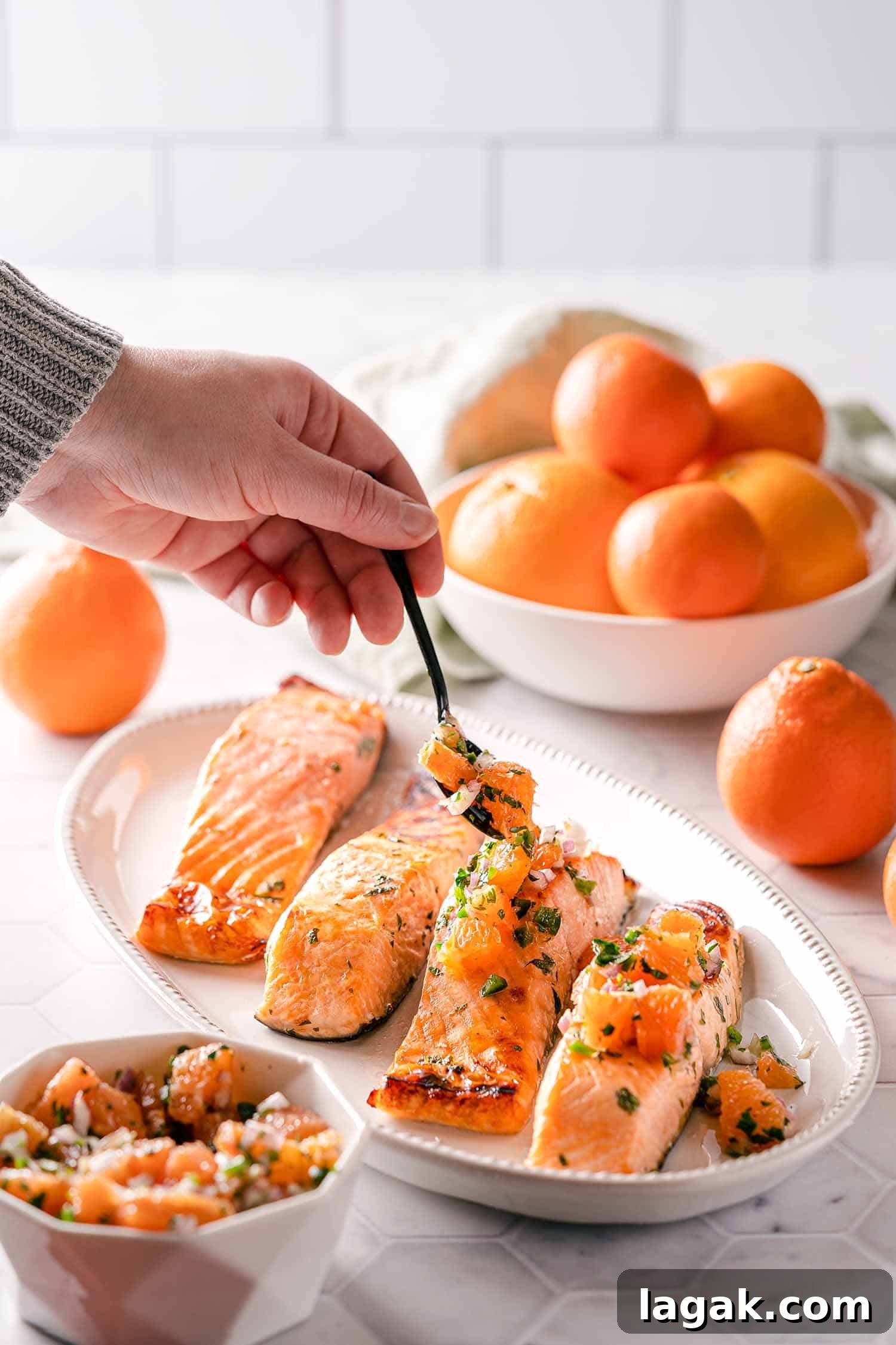 hand spooning orange salsa over broiled salmon on platter