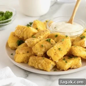 A large white serving plate with a pile of golden battered fish sticks surrounding a small glass dish of tartar sauce.