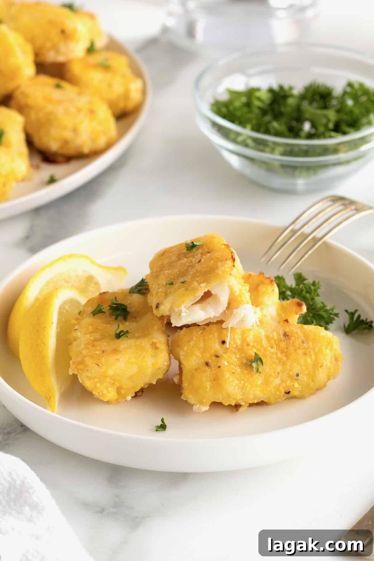 Crispy Oven-Baked Fish Sticks with Lemon Garlic Dip 3 A white plate with four fish sticks and two slices of lemon.