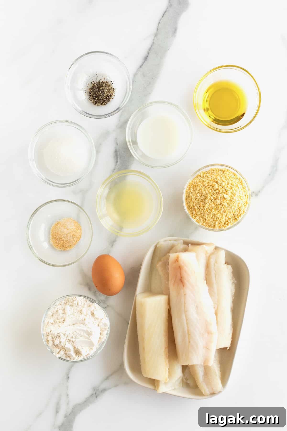 Crispy Oven-Baked Fish Sticks with Lemon Garlic Dip 8 Ingredients to make baked fish sticks in small glass dishes on a white marble counter.