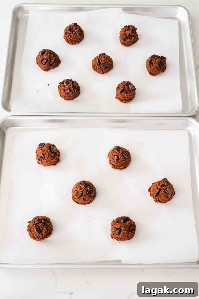 Ultimate Double Chocolate Chip Cookie Recipe for Rich, Gooey Cookies 12 Unbaked double chocolate chip cookie dough balls on a baking sheet.