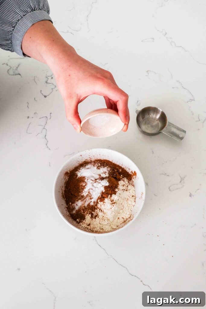 Ultimate Double Chocolate Chip Cookie Recipe for Rich, Gooey Cookies 4 A hand adds baking powder, baking soda, and salt to a bowl with flour and cocoa powder.