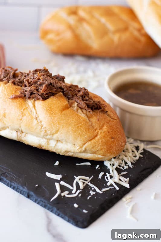 Crock-Pot French Dip Sandwich Recipe for Tender, Flavorful Beef 2 French roll containing shredded beef and cheese, au jus in bowl.