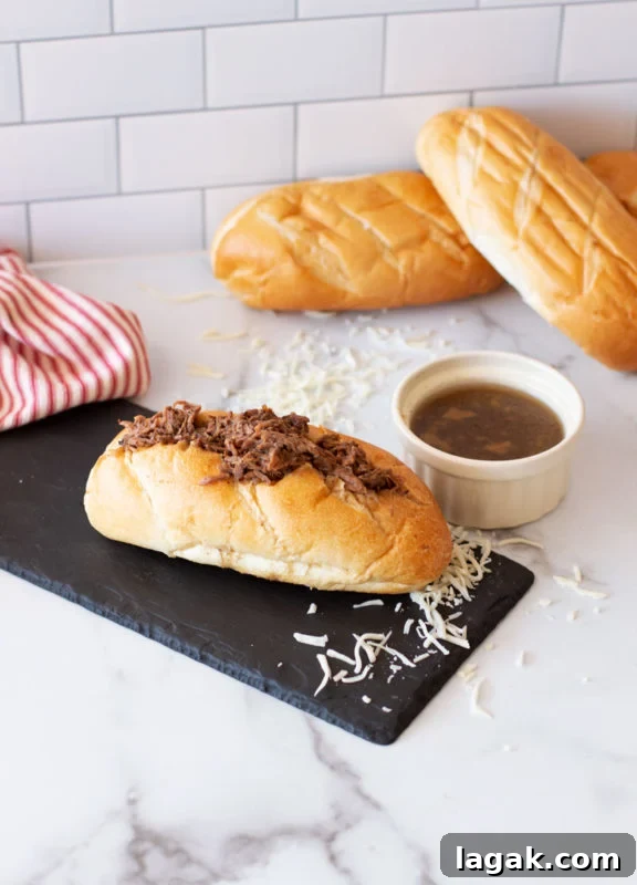 Crock-Pot French Dip Sandwich Recipe for Tender, Flavorful Beef 3 French Dip Sandwich on a counter, dipping sauce and bread on counter.