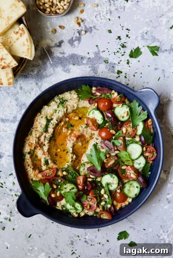 Loaded Roasted Eggplant Dip (Baba Ganoush) in blue dish with pita wedges and pine nuts.