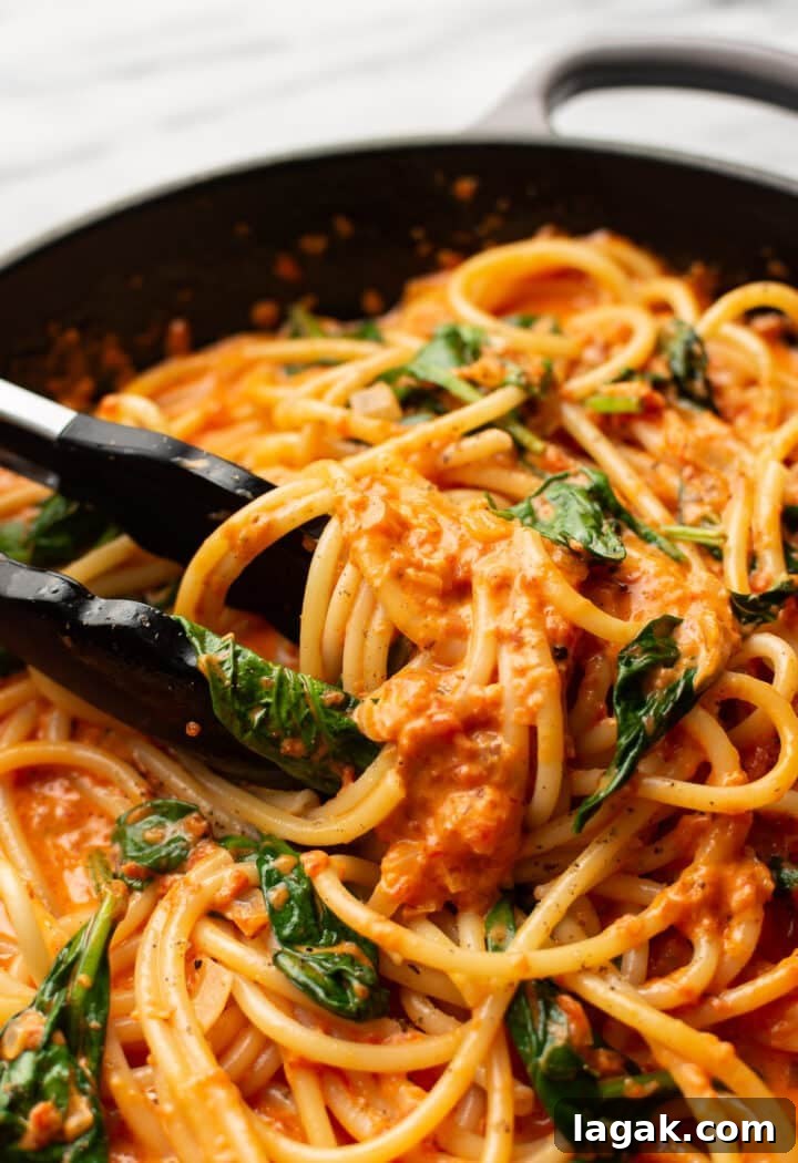 Creamy Roasted Red Pepper Pasta Recipe with Garlic and Basil 7 closeup of serving tongs in a skillet with roasted red pepper pasta