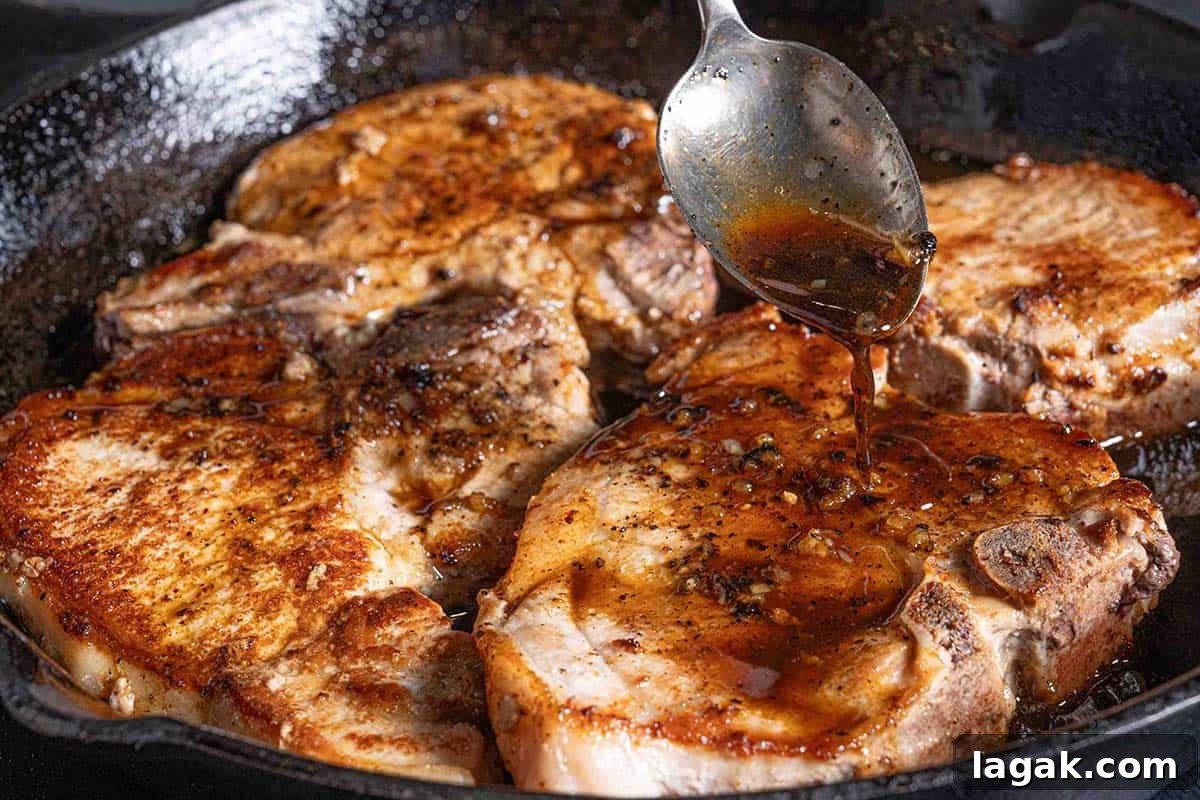 Honey Garlic Pork Chops with Sweet Glaze — Quick Weeknight Recipe 8 pork chops sizzling in a black pan being doused in honey garlic sauce with a silver spoon
