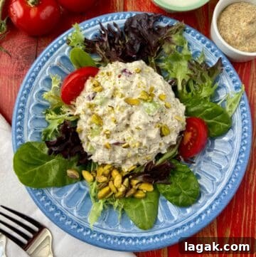 Pistachio and Poppy Seed Chicken Salad Recipe with Citrus Dressing 4 Pistachio chicken salad on a bed of greens on a blue plate with tomato wedges.