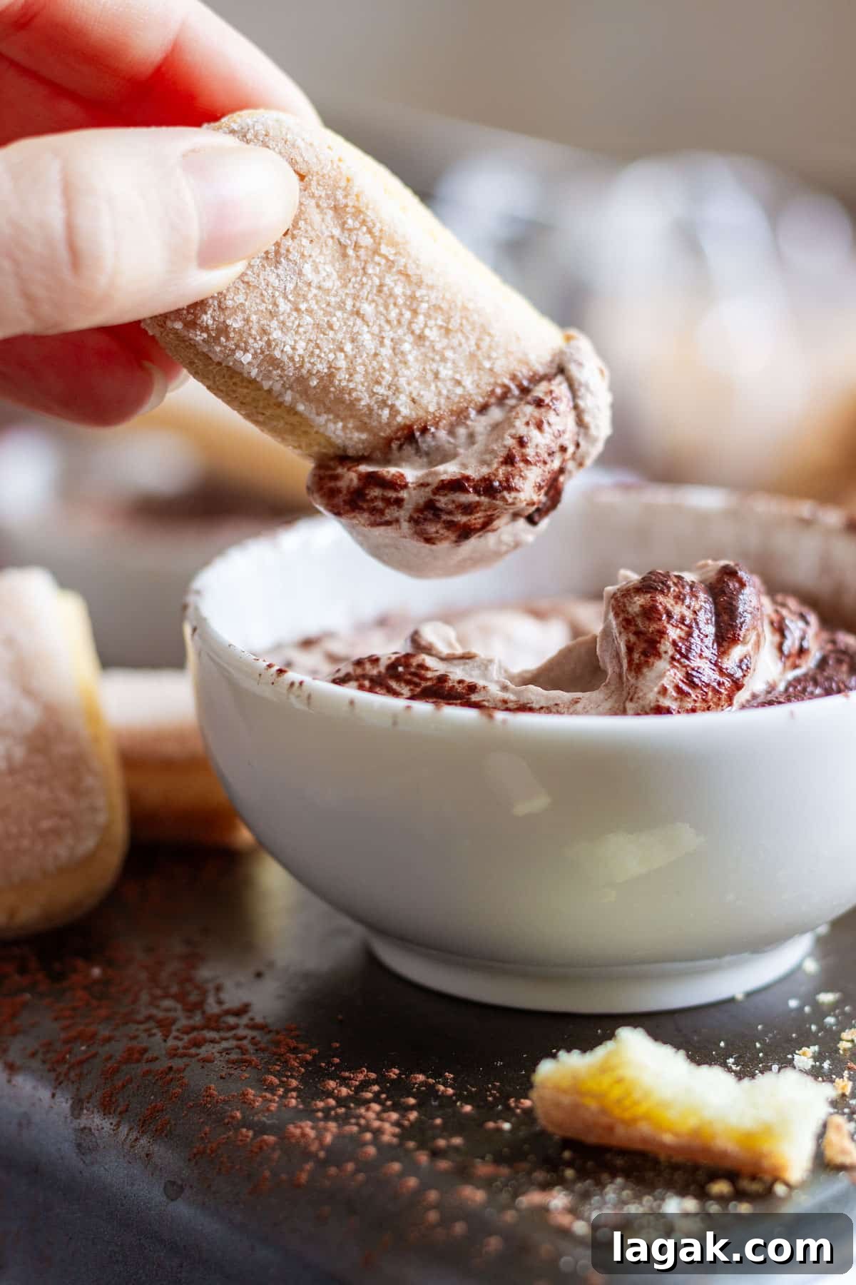 Quick Tiramisu Dip — Ready in 5 Minutes 5 A hand dips a ladyfinger into a bowl of creamy tiramisu sweet dip.