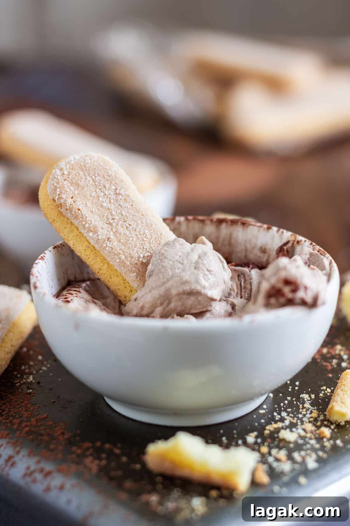 Quick Tiramisu Dip — Ready in 5 Minutes 6 A ladyfinger dipped in coffee-flavored tiramisu dip in a white bowl, with crumbs and more ladyfingers around.