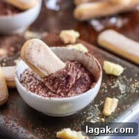 Quick Tiramisu Dip — Ready in 5 Minutes 7 A bowl of tiramisu dip with a ladyfinger dipped in it, surrounded by more ladyfingers and crumbs.
