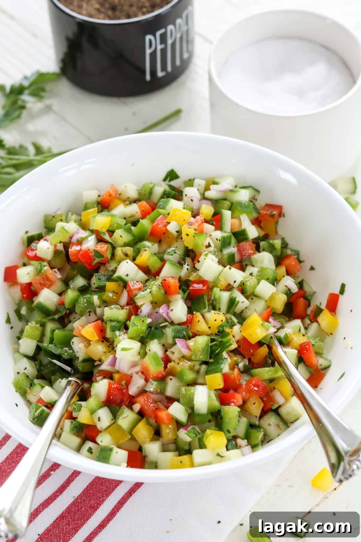 Mediterranean Cucumber and Bell Pepper Salad with Feta and Herbs 2 Chopped bell pepper cucumber salad in a white round bowl with serving spoons.