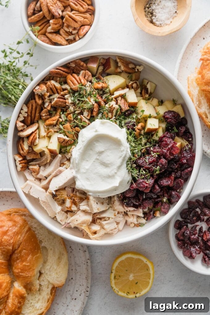 Bowl filled with the ingredients for a cranberry pecan chicken salad with Greek yogurt, added in quadrants but not yet mixed together.
