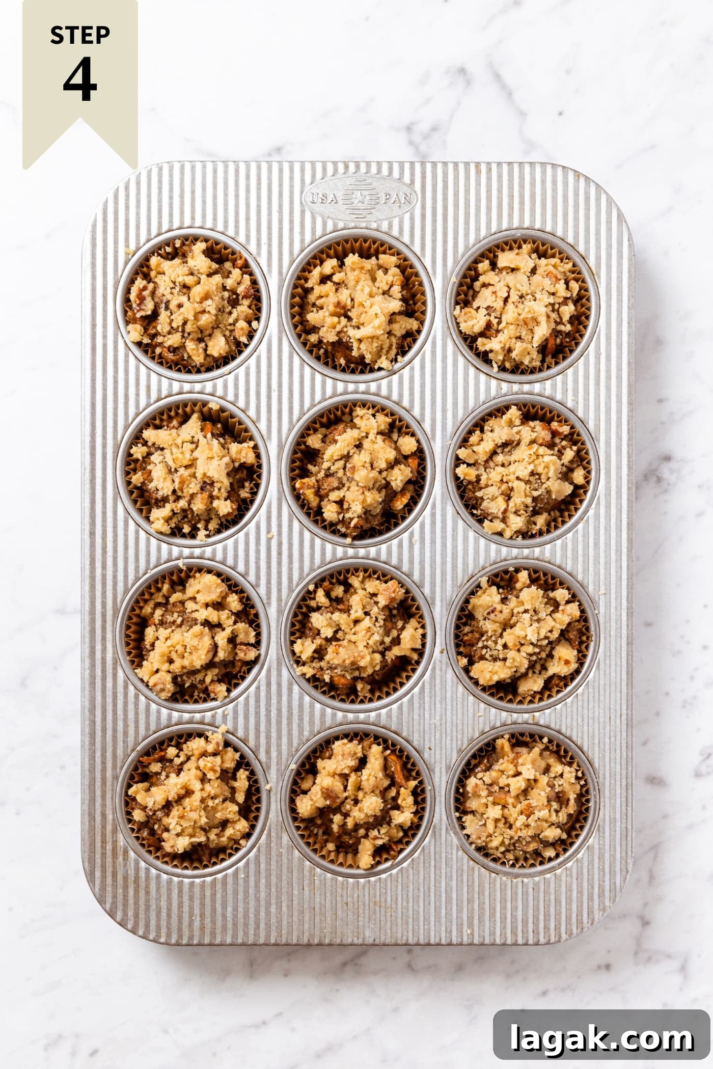 Warm Spiced Carrot Muffins with Cinnamon and Ginger 15 Muffin tin pan resting on white marble surface filled with unbaked carrot muffins with streusel topping.