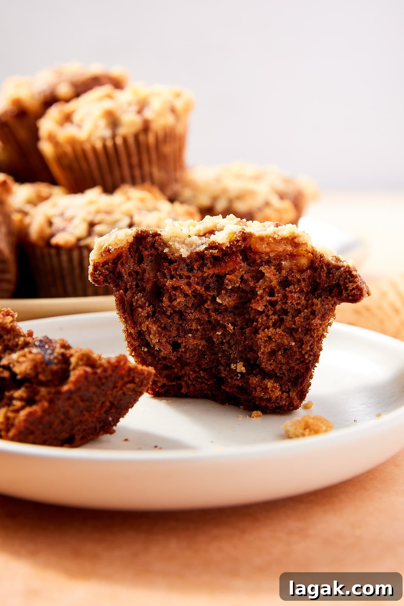 Warm Spiced Carrot Muffins with Cinnamon and Ginger 18 White plate with spiced carrot muffin sitting on it after being broken in half with dark interior texture and streusel topping.