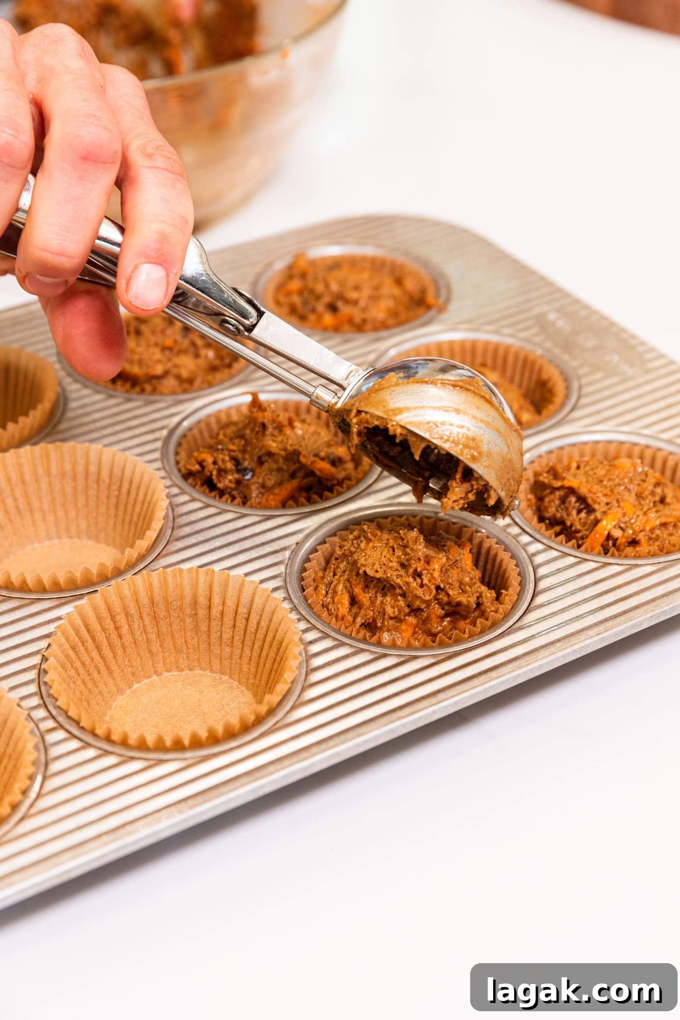Warm Spiced Carrot Muffins with Cinnamon and Ginger 10 Hand using cookie scoop to place dollops of batter into a muffin pan fitted with muffin cups.