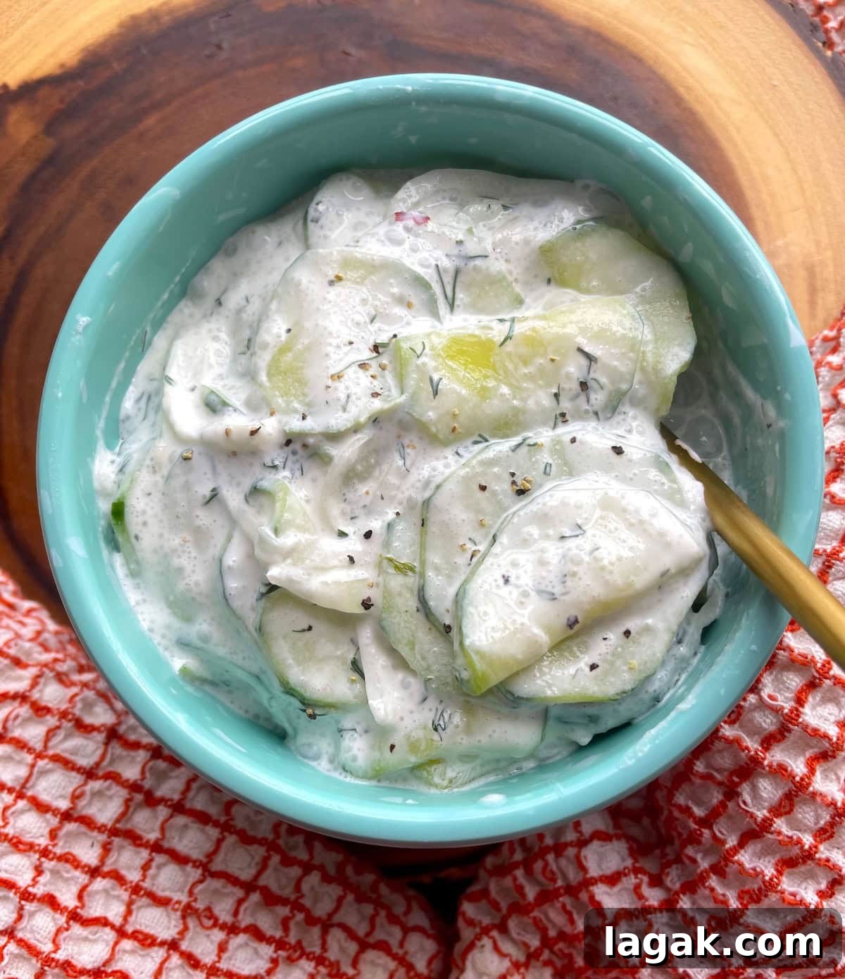 Creamy German Gurkensalat Recipe: Classic Cucumber Salad with Dill 10 A small turquoise bowl of creamy cucumber salad with fresh dill and a gold spoon.