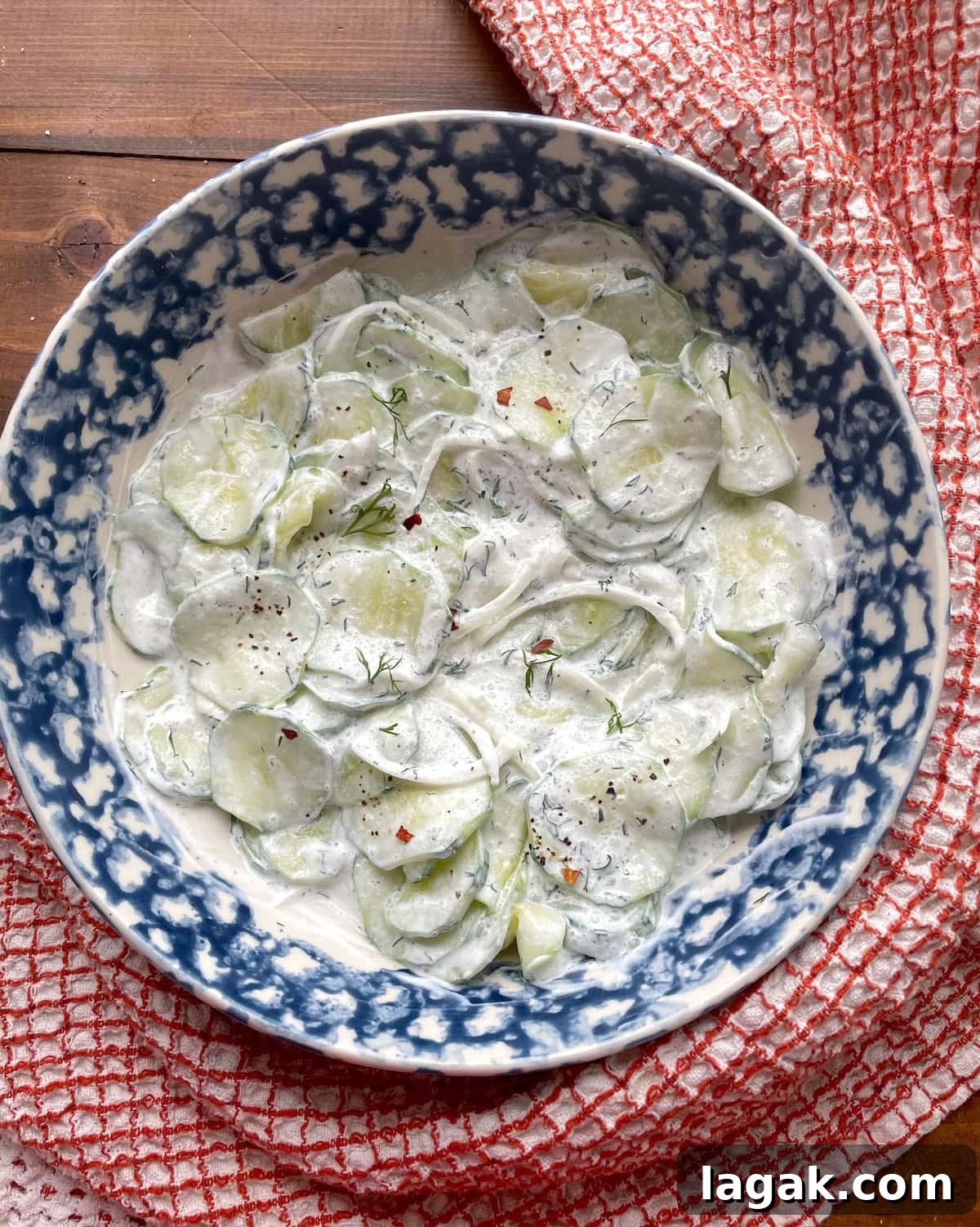 Creamy German Gurkensalat Recipe: Classic Cucumber Salad with Dill 12 A blue bowl of creamy cucumber salad with sliced onions, fresh dill, and red pepper flakes.