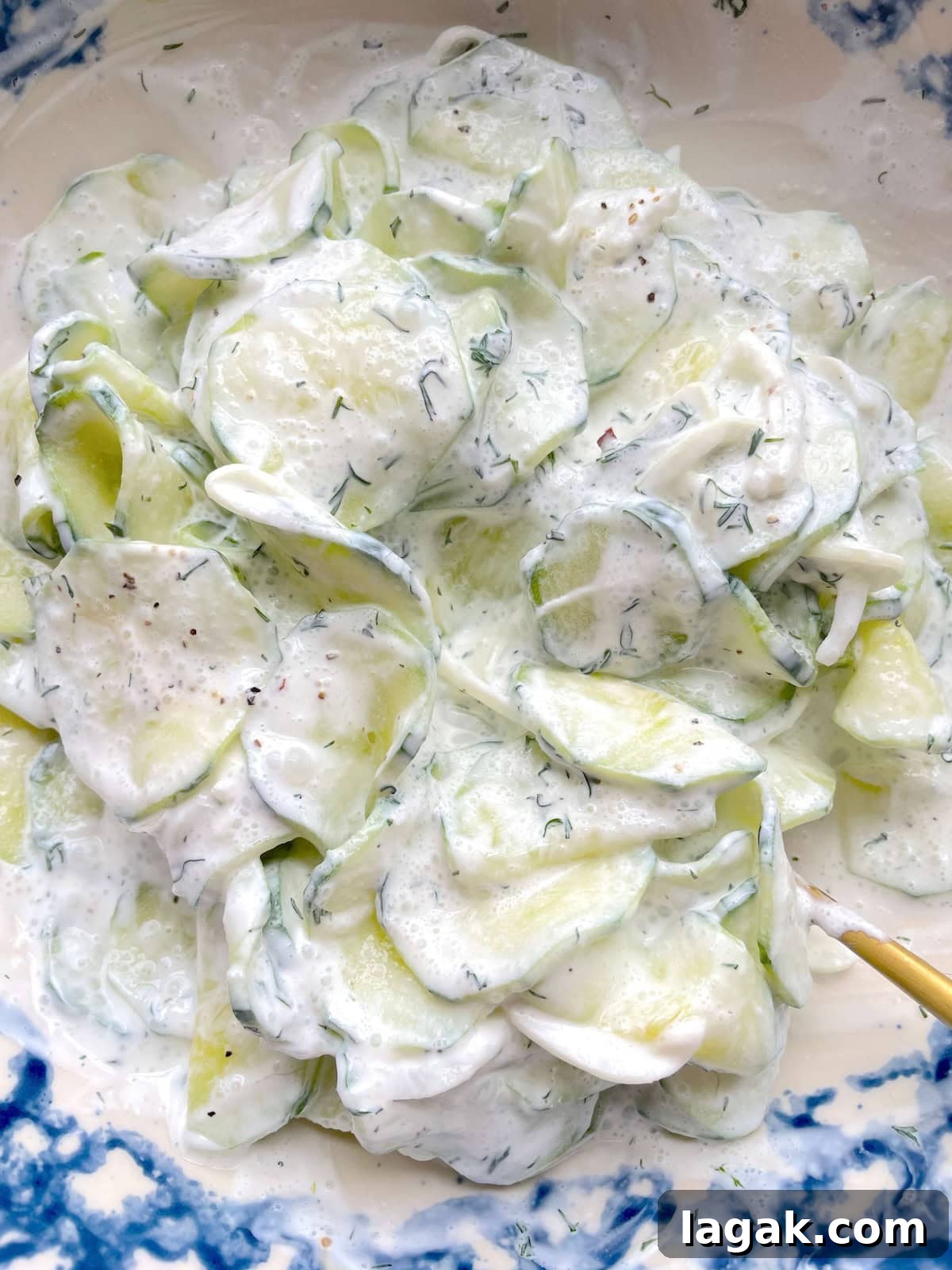 Creamy German Gurkensalat Recipe: Classic Cucumber Salad with Dill 9 A blue bowl of creamy cucumber salad with fresh dill and a gold spoon.