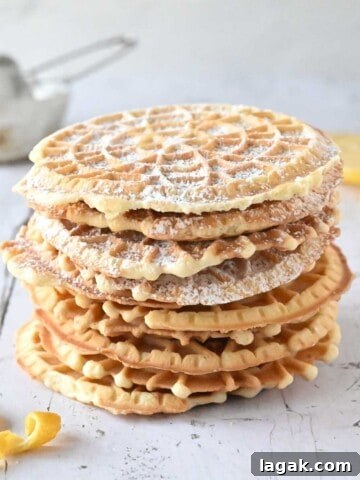 Lemon pizzelles stacked on top of each other on white wood with lemon in the background.