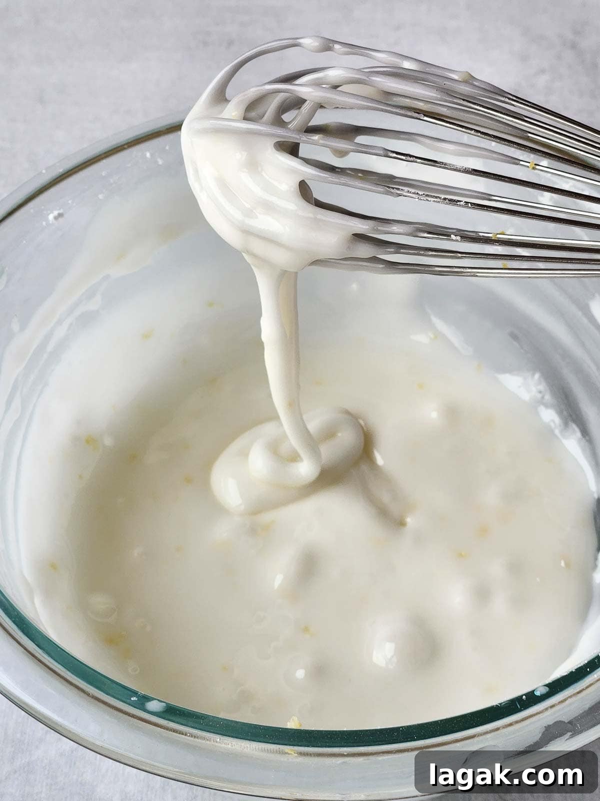 Italian Lemon Drop Cookies Recipe — Zesty Citrus Biscotti-Style Treat 9 White icing dripping off a whisk into a bowl.