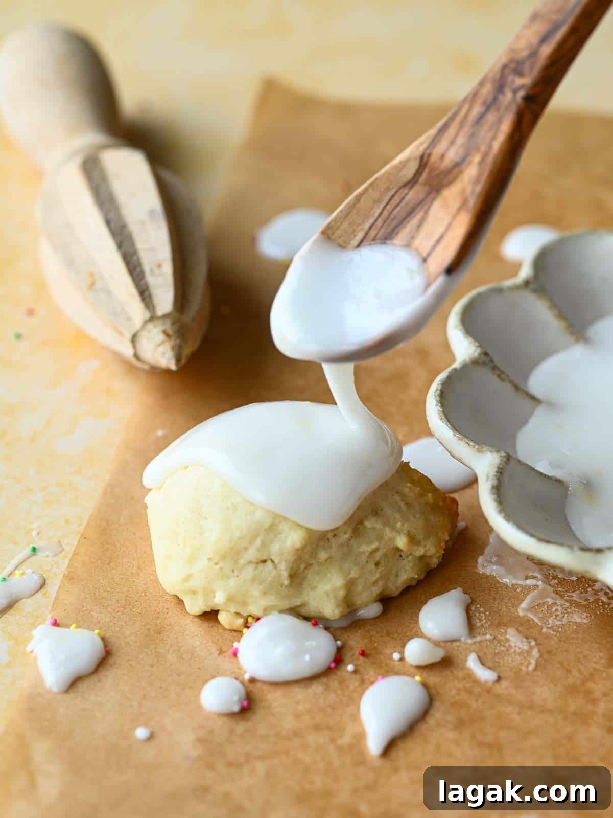 Italian Lemon Drop Cookies Recipe — Zesty Citrus Biscotti-Style Treat 10 Lemon icing being dripped by a spoon over a cookie on top of brown parchment paper.