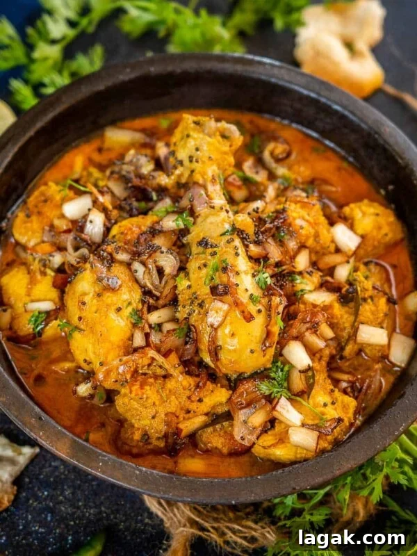 Chicken Angara Recipe: Spicy Grilled Chicken with Smoky Sauce 19 A black bowl filled with spicy Malabar Chicken Curry, garnished with chopped onions and herbs.