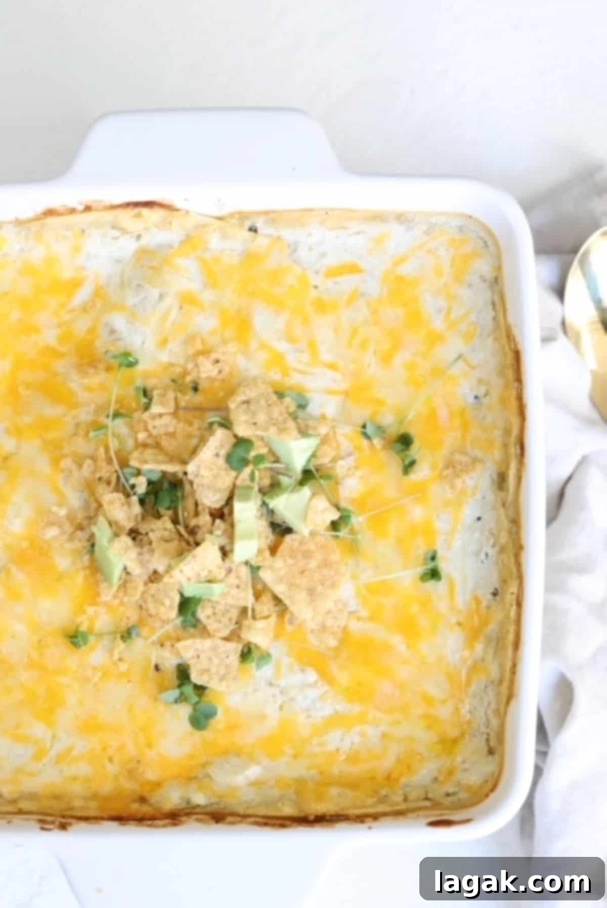 Top view of a layered enchilada casserole topped with crushed tortilla chips, small pieces of avocado, and microgreens.