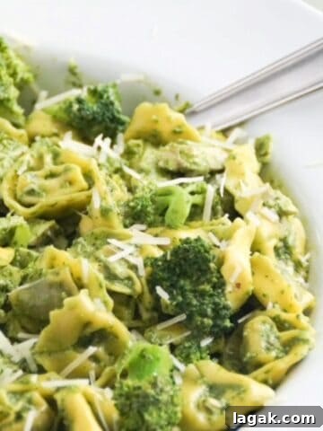 Pesto with tortellini, chicken, and broccoli in a large white serving bowl with a spoon.