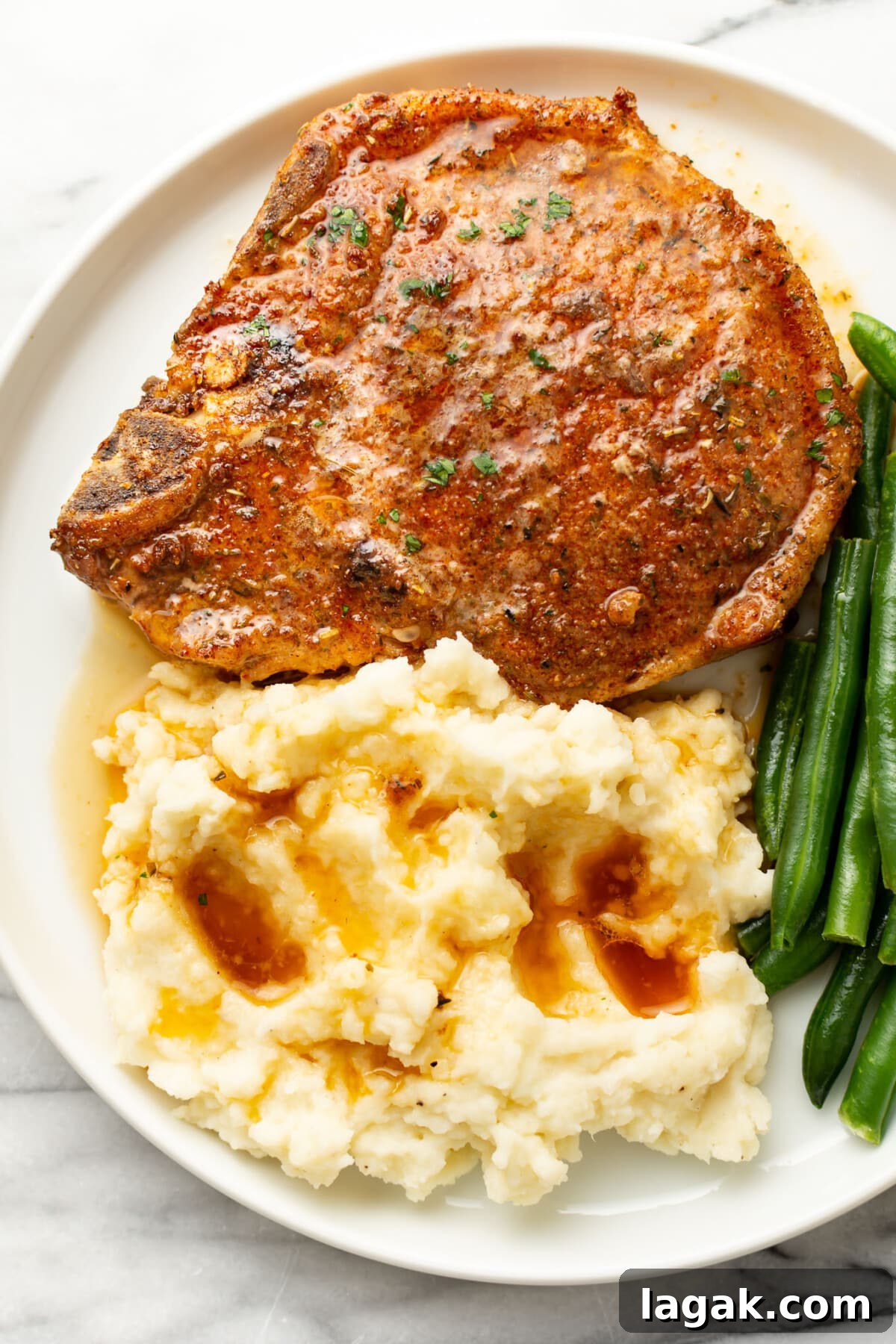 Juicy Oven-Baked Pork Chops with Garlic and Herbs 6 a plate with a baked pork chop, mashed potatoes, green beans, and sauce