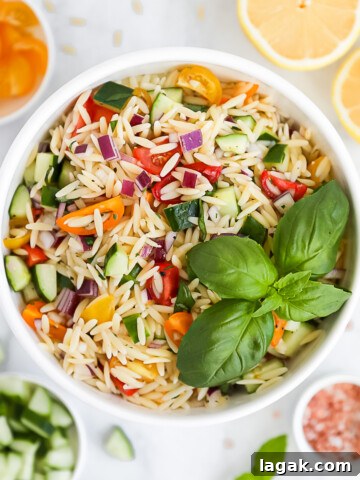 An overhead picture of a bowl of fresh pasta salad filled with fresh vegetables and with a bunch of basil leaves on top.