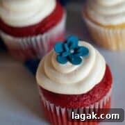 Two simple Red Velvet Cupcakes with delicious cream cheese frosting and a blue flower on top.
