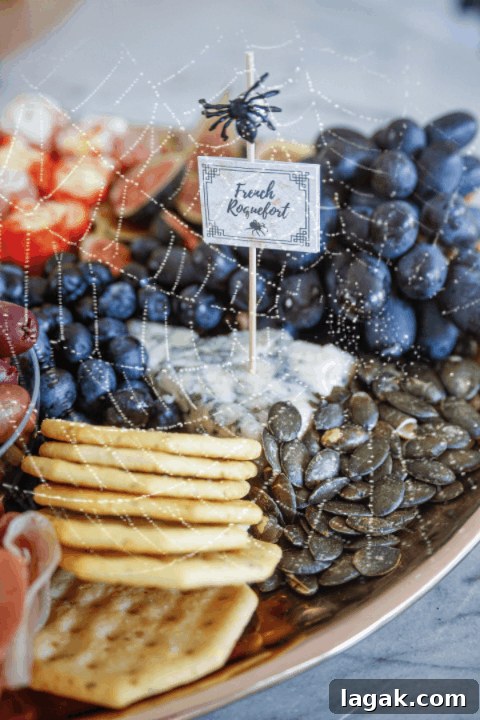 a Halloween charcuterie board with crackers, grapes, pumpkin seeds and a printable cheese label that says French roqueford 