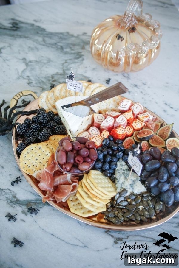 a Halloween meat and cheese tray styled with toy spiders and a glass pumpkin