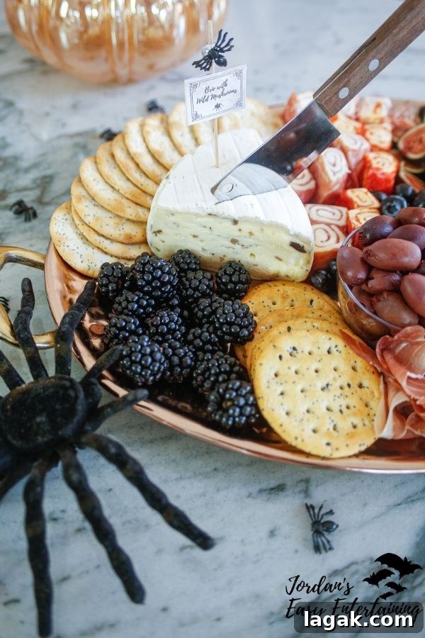 a Halloween charcuterie board with a wedge of wild mushroom brie with a butcher knife cheese knife, crackers, blackberries, grapes and styled with a toy spider 